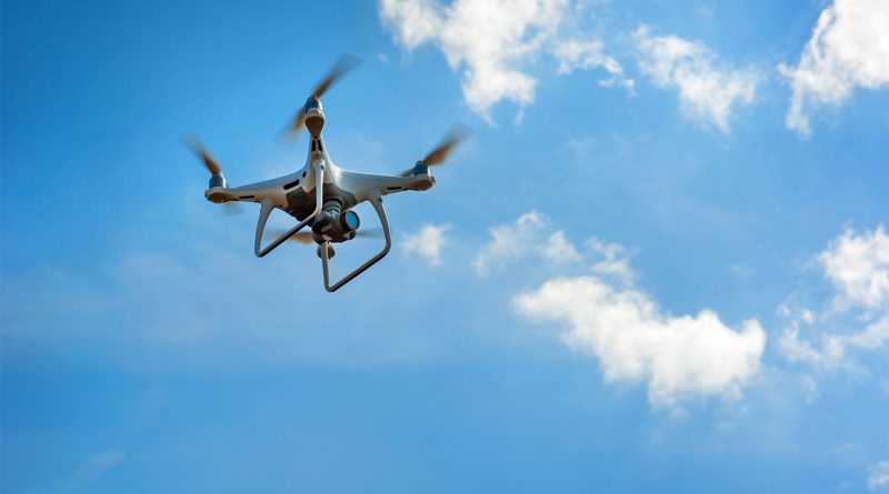 Image of a drone flying in the sky with blue skies and clouds behind it to support drone technology article